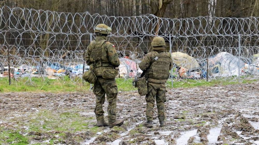 Польские пограничники смотрят на лагерь нелегальных мигрантов на беларуской стороне в в Беловежской пуще. Фото: rp.pl.