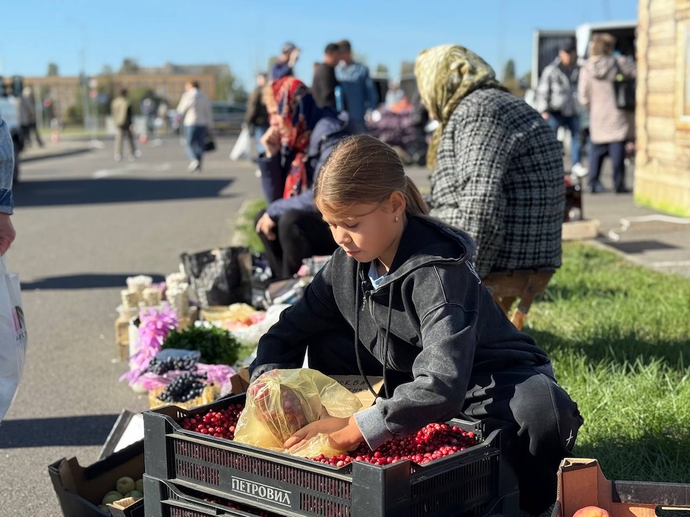 Девочка набирает в банку клюкву на осенней сельскохозяйственной ярмарке в Бресте.