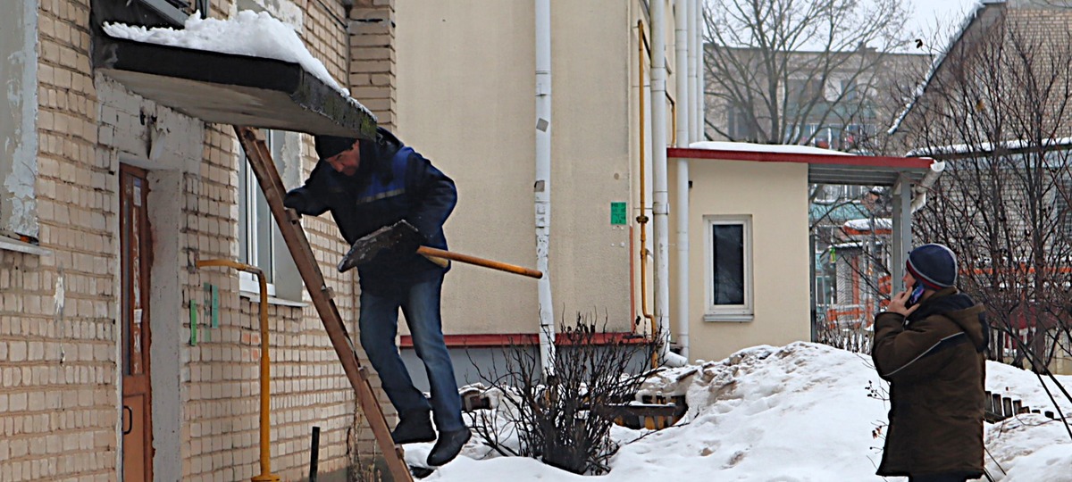 Коммунальщик чистит от снега козырек подъезда, который потом рухнет. Фото: Kraj.by